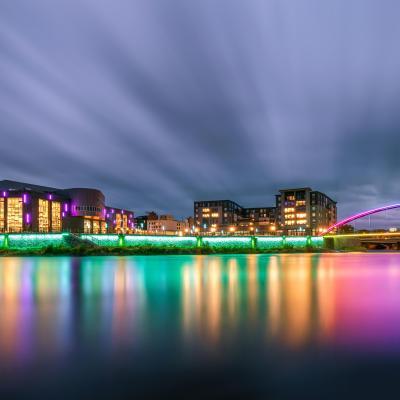 Pablo Center as viewed from across the river at night with the bridge lit up.